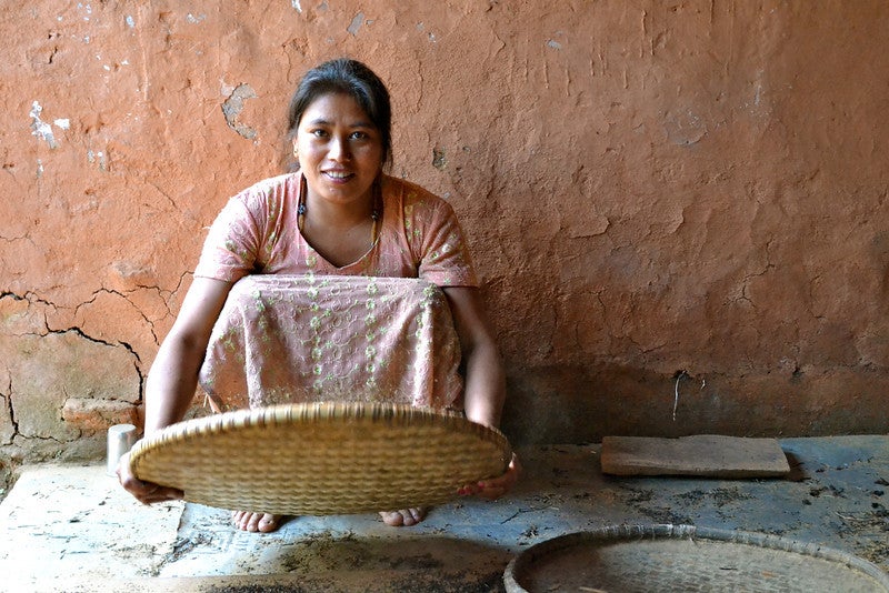 A woman crouches to collect shallow baskets of dried tea