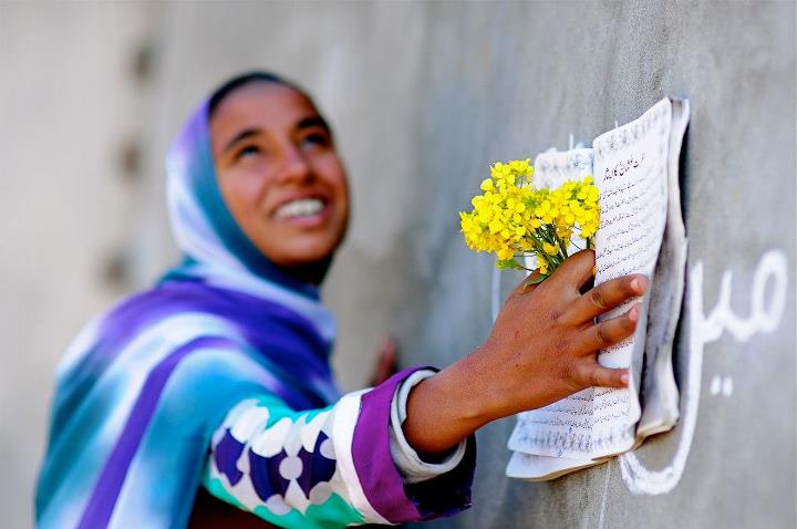 A woman smiles with flowers and a book.