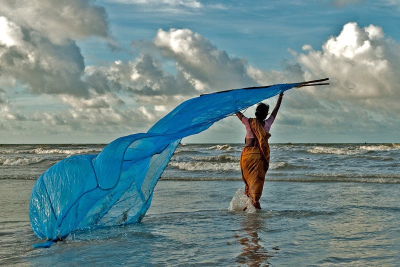 A woman fishes with a net in the ocean