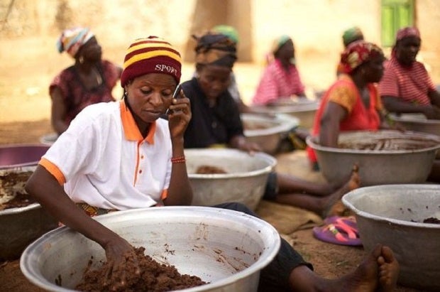 A woman in Ghana uses a phone while making food.