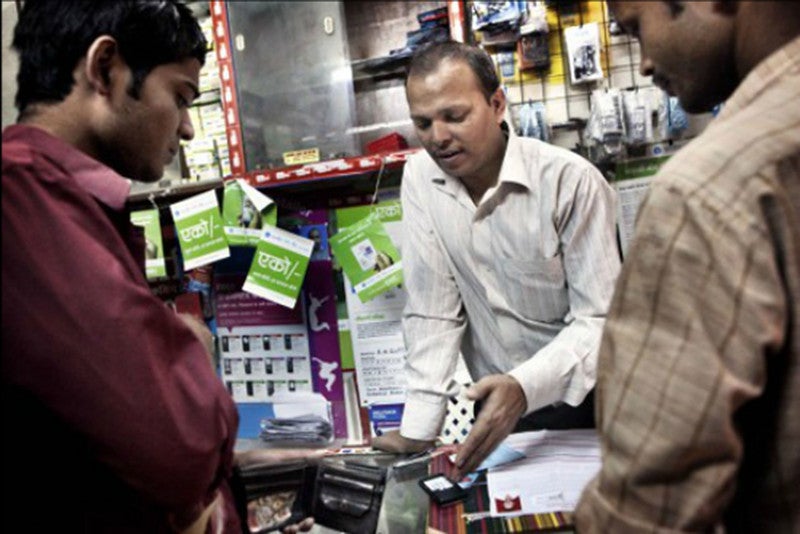 A shopkeeper shows two men how to use a mobile phone for banking.