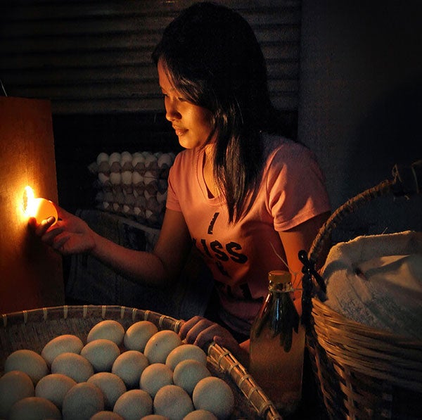 An egg vendor holds an egg up to a light.