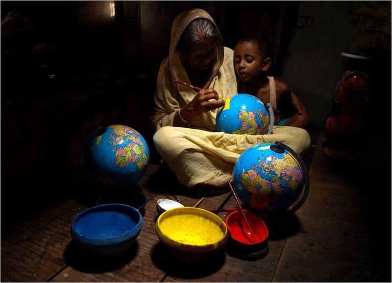 A grandmother works at painting globes while holding a child