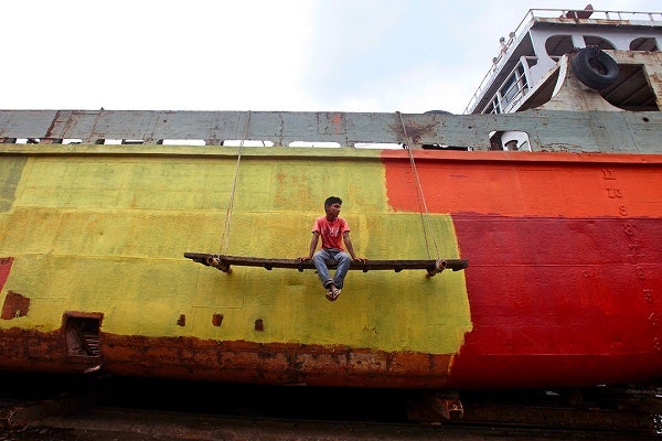 A man painting a boat takes a rest and hangs off the side of the deck