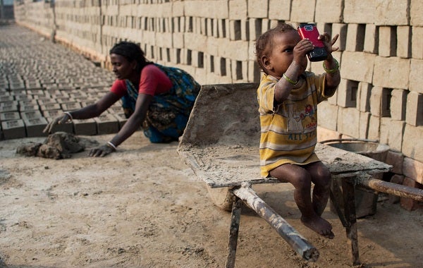 A child plays with a mobile device with his mother working in the background
