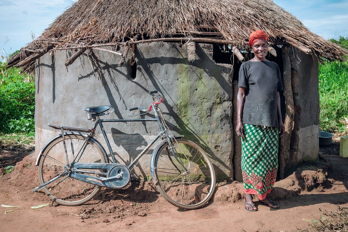 Jennifer, who lives in a village in northern Uganda, stands next to a bicycle she financed through a social enterprise called BAP. She and her daughter use the bicycle to access the nearest health clinic, which is several miles away.