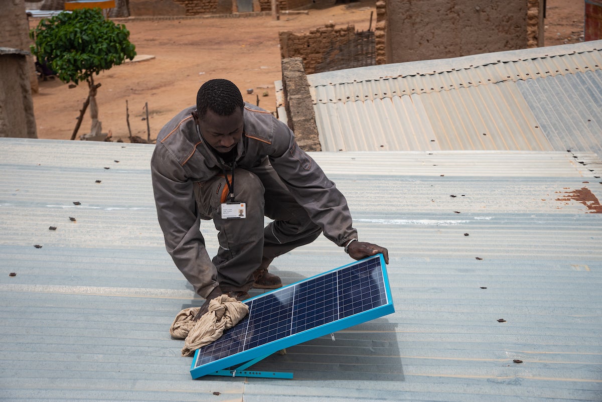 An employee of Orange Energie — a PAYGo solar provider in Mali — cleans a rural customer's solar panel. Photo: Nicolas Réméné