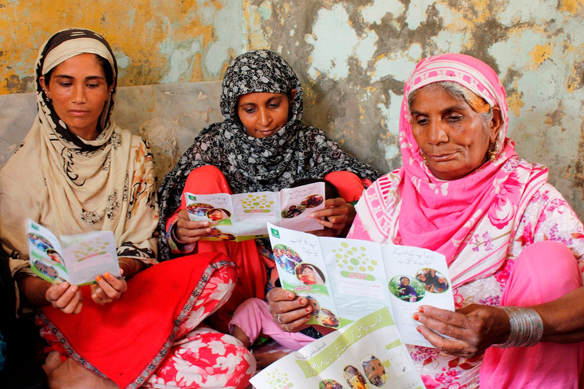 A group of women read about a savings program in Pakistan.