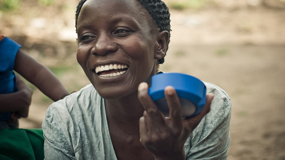 A smiling woman holds a solar light. Photo taken by Off: Grid Electric.