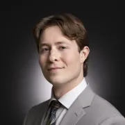 headshot of man in gray suit against dark background