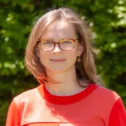 headshot of woman in red shirt against greenery