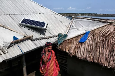 South Asian woman on the phone in front of rural building with solar panels on roof