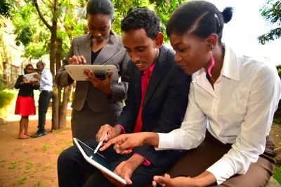 A group of people are looking at a tablet while sitting outside