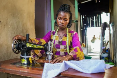 a young African woman in colorful clothing working a sewing machine at a desk