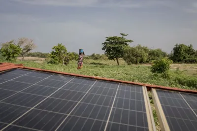 an African woman carrying a bucket on her head walks past a solar panel