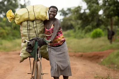 A Ugandan smallholder walks along a dirt road with her bike.