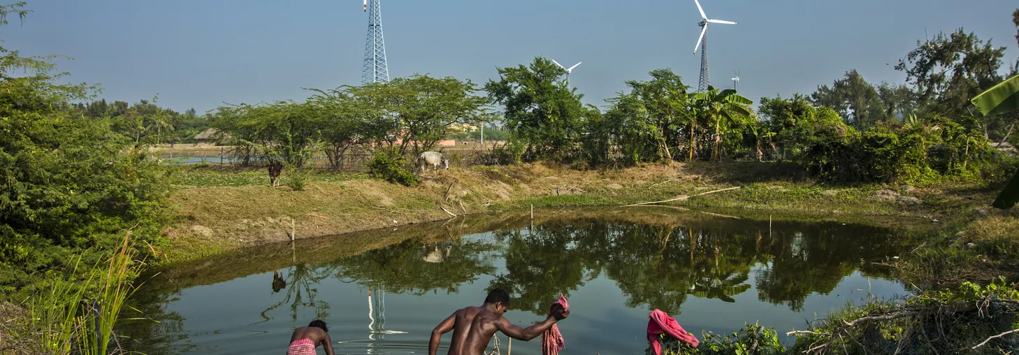 Two men washing clothes in a pond with windmills in the background