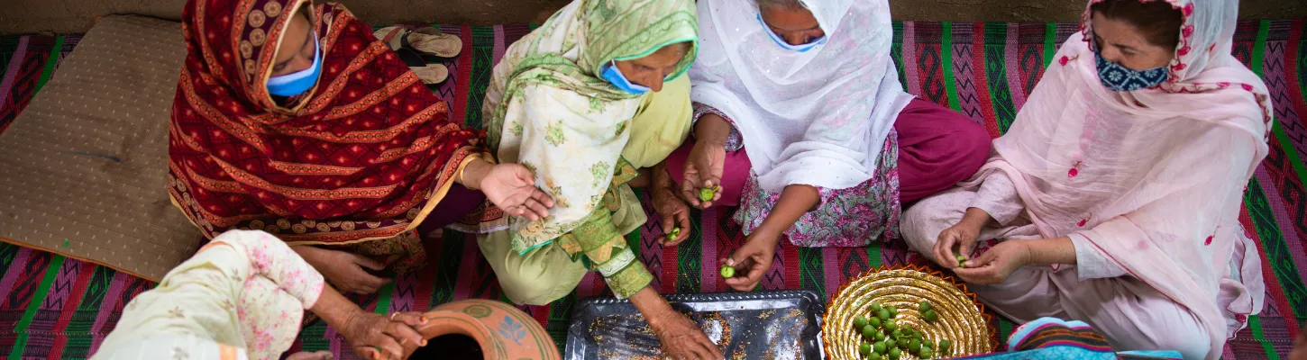 a group of women in pakistani clothes sitting on the floor making pickled herbs and spices