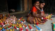A mother makes wooden dolls while her child watches