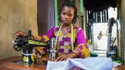 a young African woman in colorful clothing working a sewing machine at a desk