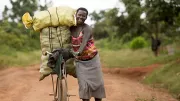 A Ugandan smallholder walks along a dirt road with her bike.