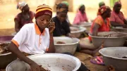 A woman in Ghana uses a phone while making food.