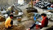 A girl studies on her computer while her family works on pottery