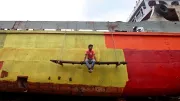 A man painting a boat takes a rest and hangs off the side of the deck