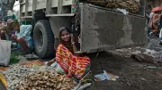 A woman uses a phone while selling garlic and ginger from a food stall.