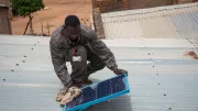 An engineer with Orange Energie, a PAYGo solar provider in Mali, cleans a rural customer's solar panel. Photo: Nicolas Réméné